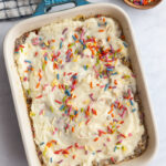 Casserole dish of baked oats topped with cream frosting and sprinkles with a bowl of sprinkles on the side