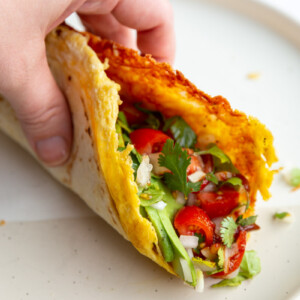 hand holding up a breakfast taco with lots of veggies in it