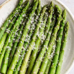 Cooked asparagus on a plate with a sprinkle of parmesan cheese.
