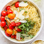 White bowl filled with pasta, tomatoes, basil and parmesan cheese.