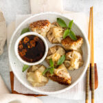 Vegan dumplings served on a white plate with dipping sauce.