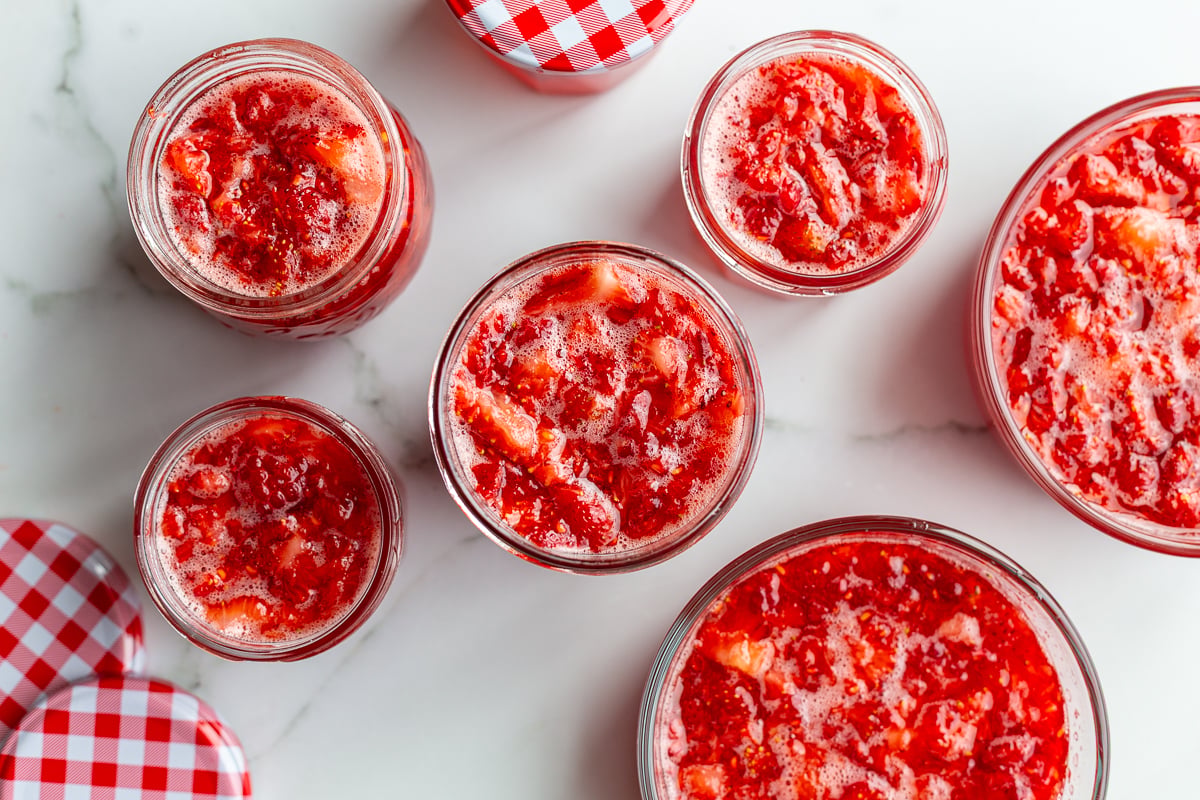 Strawberry freezer jam poured into small glass jars with red gingham lids