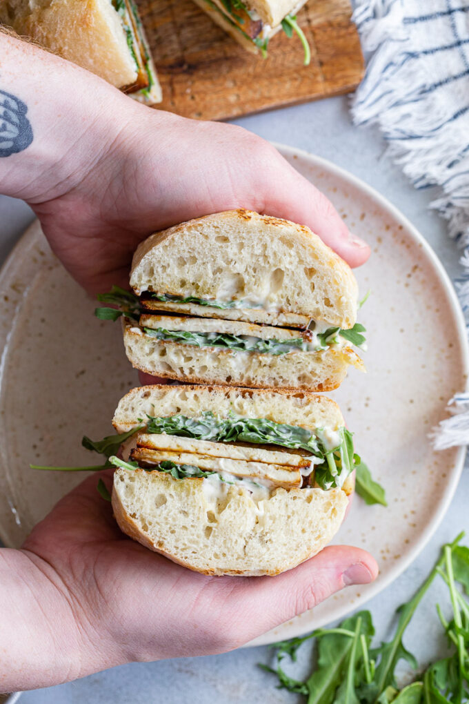 Hand serving a sandwich on a white plate.