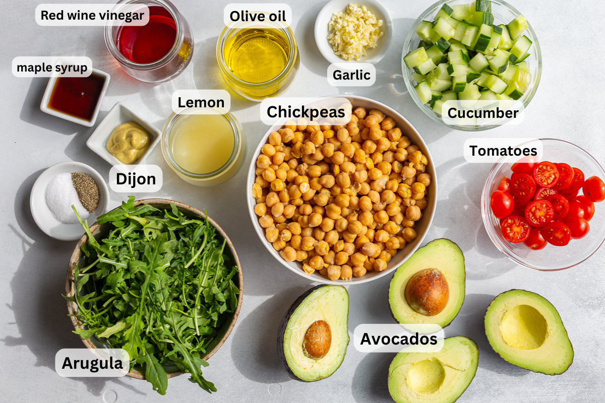ingredients needed to make chickpea avocado salad indlugin chickpeas, avocado, arugula, olive oil, tomatoes, cucumber, and dijon