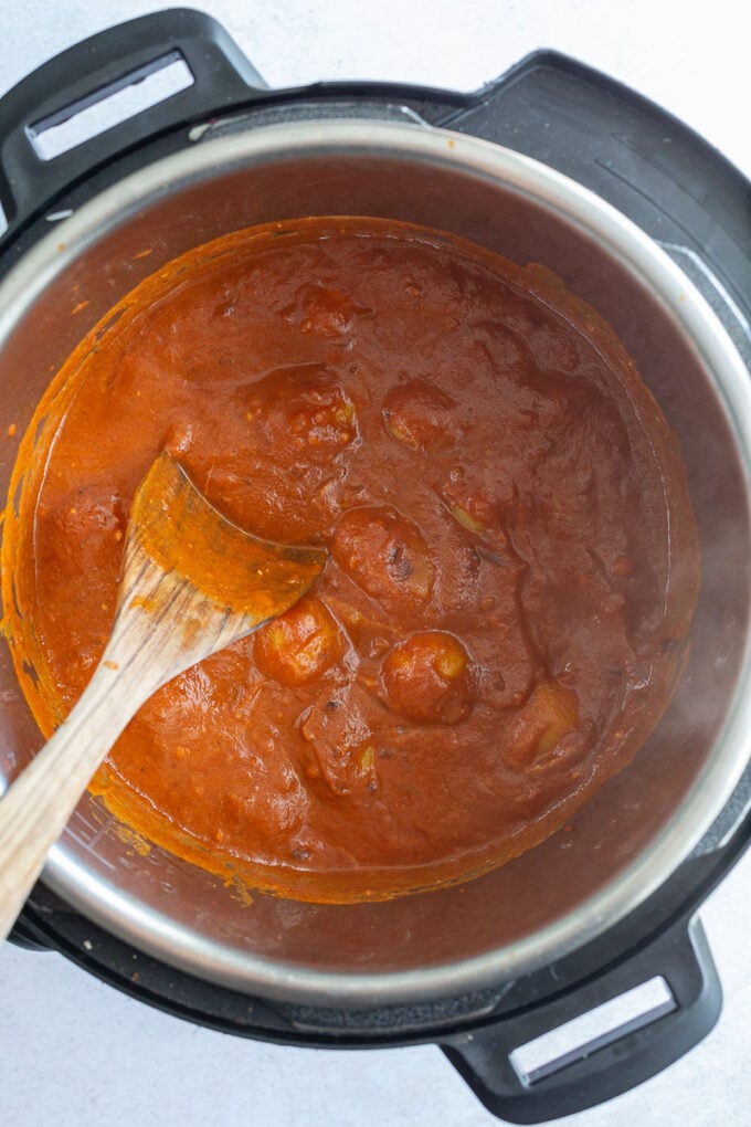 Stirring potatoes into a tomato sauce.
