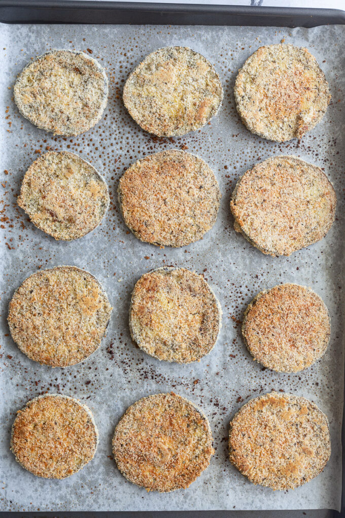 Breaded eggplant slices on a sheet pan.