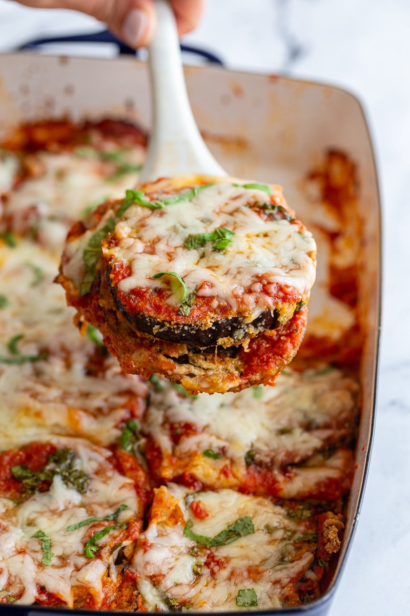 Serving a portion of eggplant parmesan out of a white baking dish.