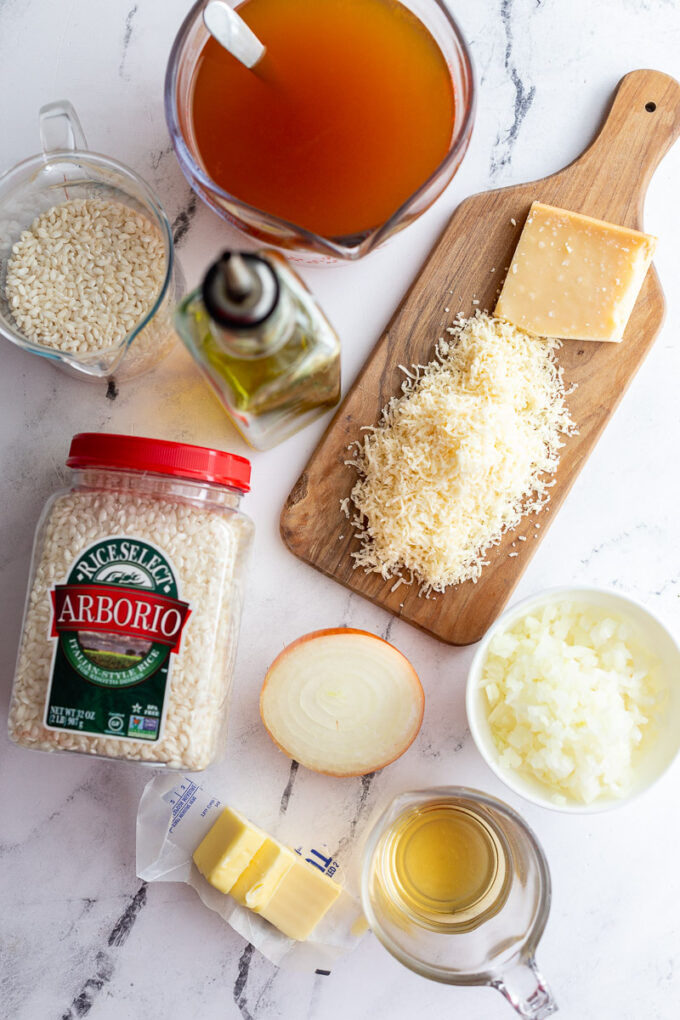 Uncooked arborio rice, parmesan cheese, olive oil and broth portioned into small bowls.