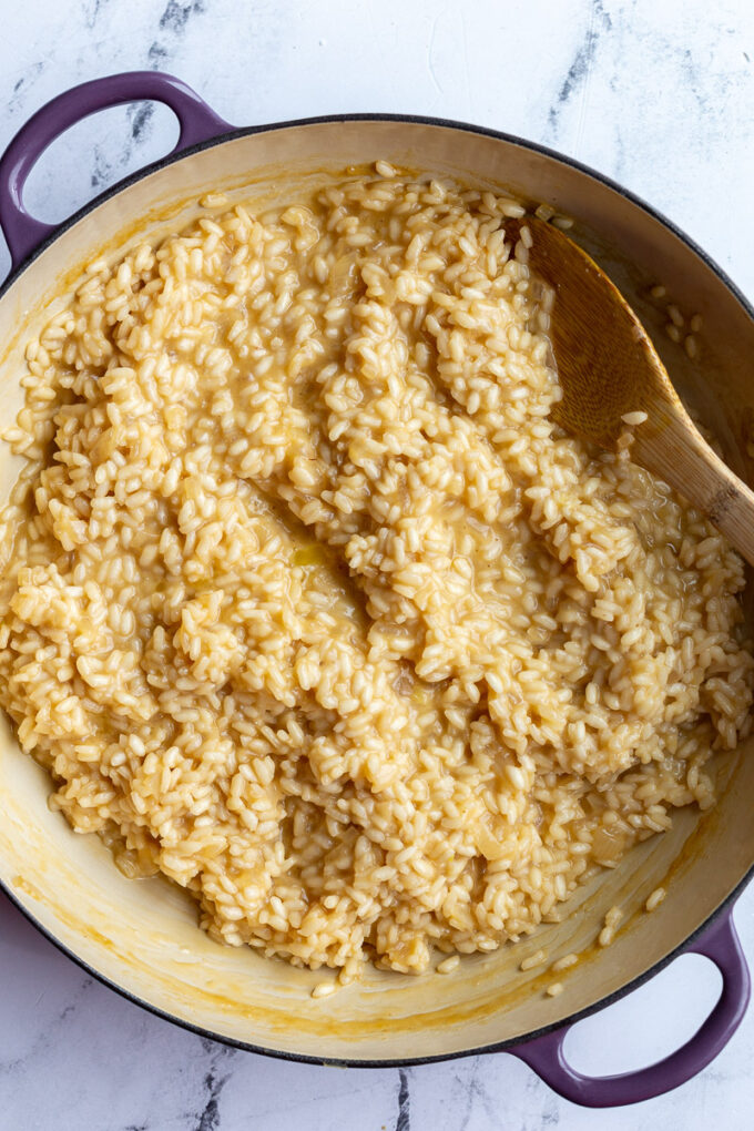 Using a wooden spoon to stir risotto in a large pot.