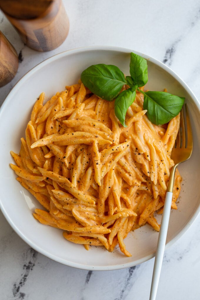 Spiral pasta in a roasted red pepper sauce in a large wide bowl with basil on top
