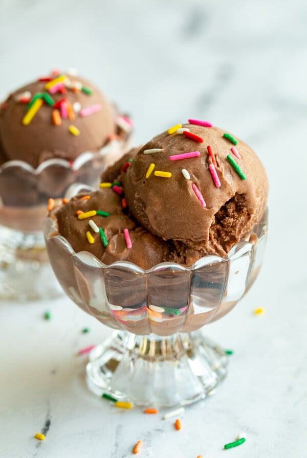 chocolate ice cream in a clear dish and topped with colorful sprinkles