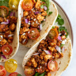 3 flour tortilla filled with tofu taco meat and topped with cherry tomatoes, cilantro, onion, and feta