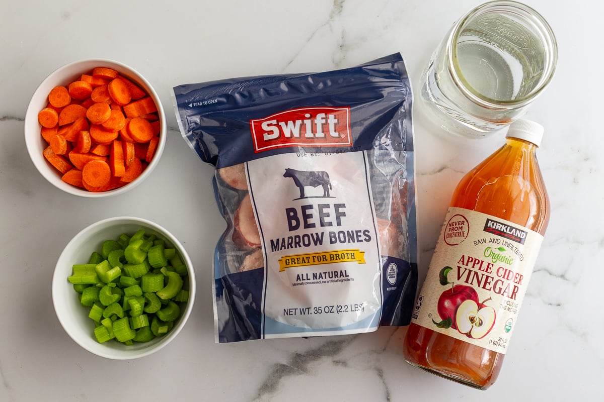 ingredients laid out that are needed for dog bone broth including carrots, celery, bones, water, and apple cider vinegar