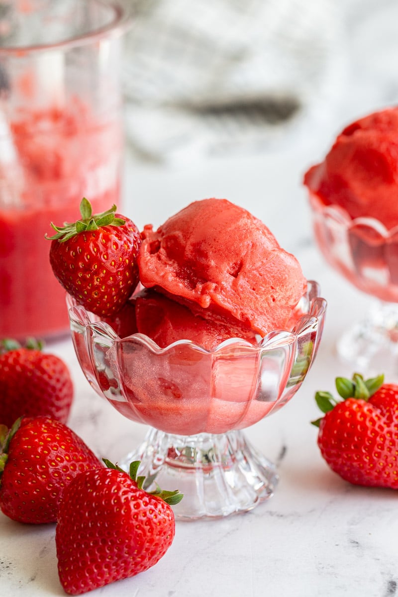 Strawberry sorbet in an ice cream dish with strawberries around the scene
