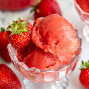 Strawberry sorbet in an ice cream dish with strawberries around the scene