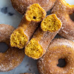 cinnamon sugar baked pumpkin donuts on a tray. 1 donut is cut in half so you can see the inside