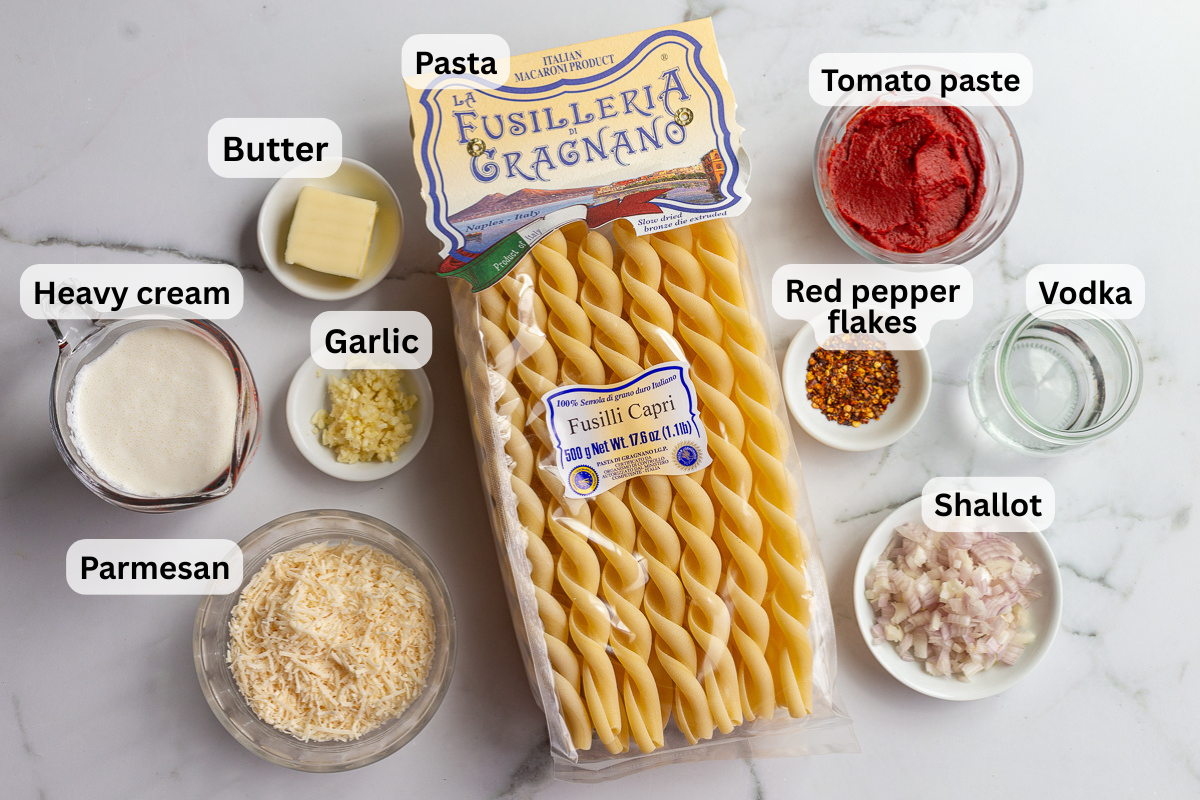 Labeled ingredients for Gigi Hadid pasta including pasta, tomato paste, vodka, heavy cream, garlic, shallot, butter, red pepper flakes, and parmesan on a marble counter.