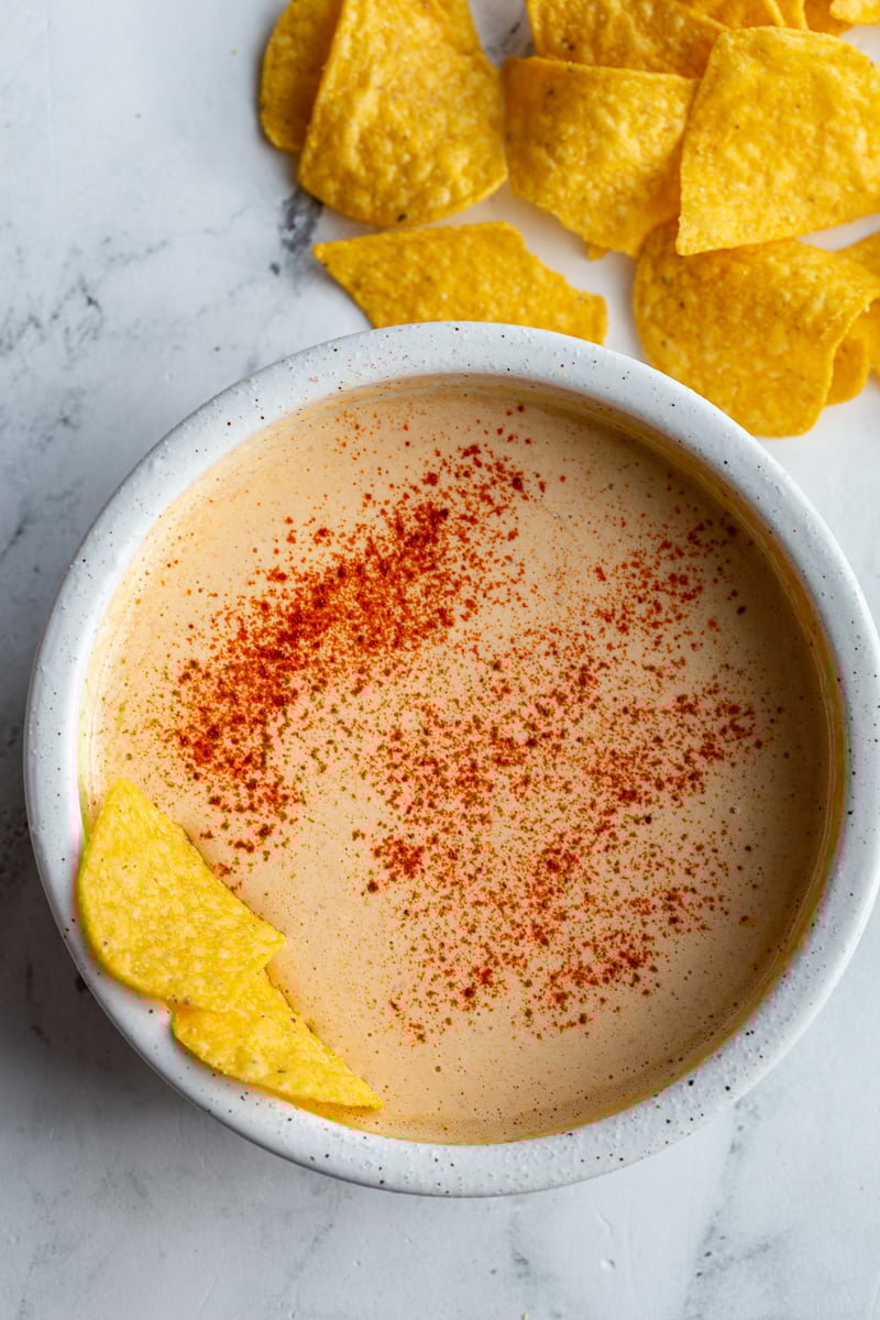 bowl of cottage cheese queso sprinkled with paprika and a few chips are hanging out the side of the bowl