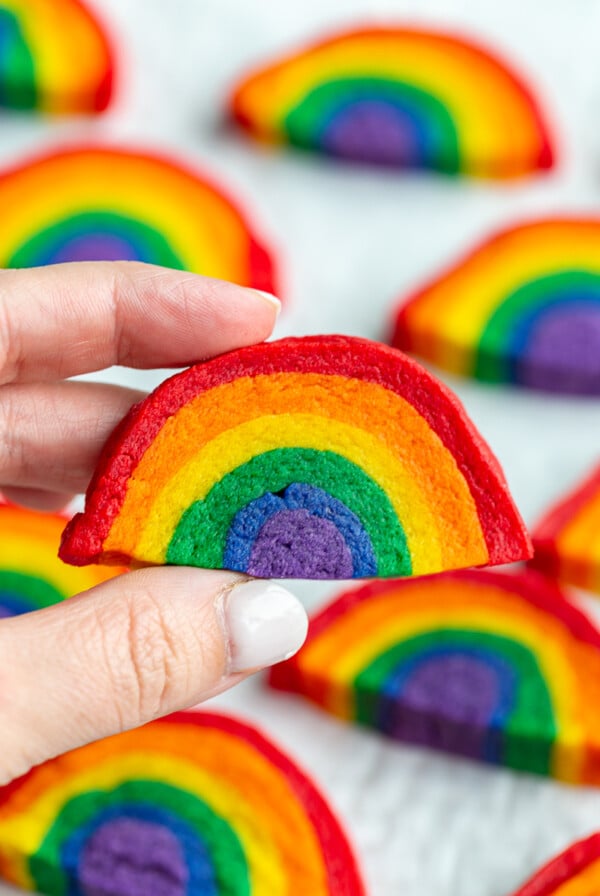 hand holding up a rainbow sugar cookie with more cookies in the background
