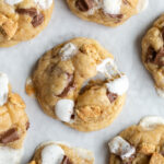 s'mores cookies on a baking tray. One of the cookies is puled apart so you can see the gooyness of he marshmallow on the cookies