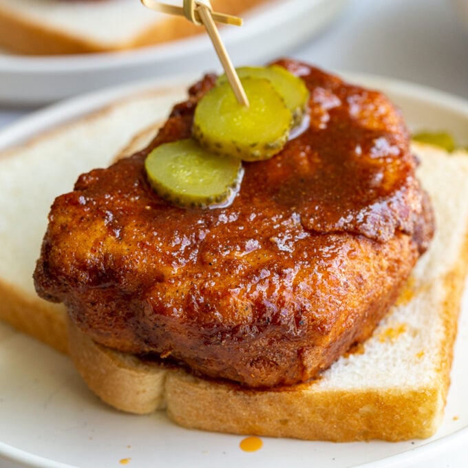 bread and fried piece of tofu covered in Nashville hot chicken sauce. It's sitting on top of slices of white bread and topped with slices of pickel