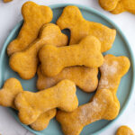 Pumpkin dog biscuits shaped like dog bones on a plate.