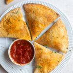 large pizza pockets made out of tortillas sitting on a plate with a cup of marinara on the side