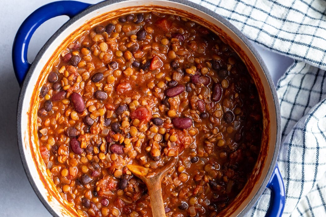 lentil chili in a large navy blue pot with a wooden spoon hanging out the side
