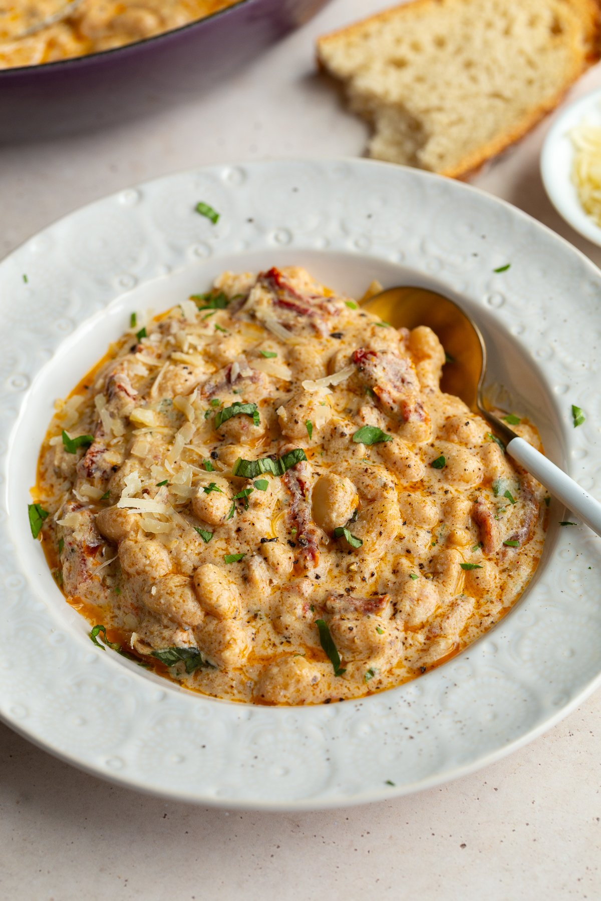 high protein marry me butter beans in a white bowl with crusty bread in the background