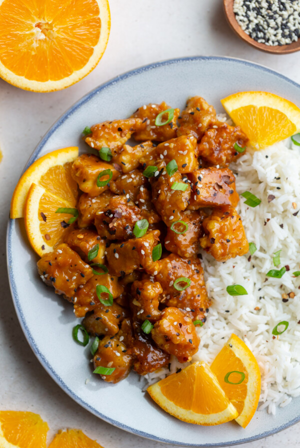 orange tofu on a plate with rice and orange slices