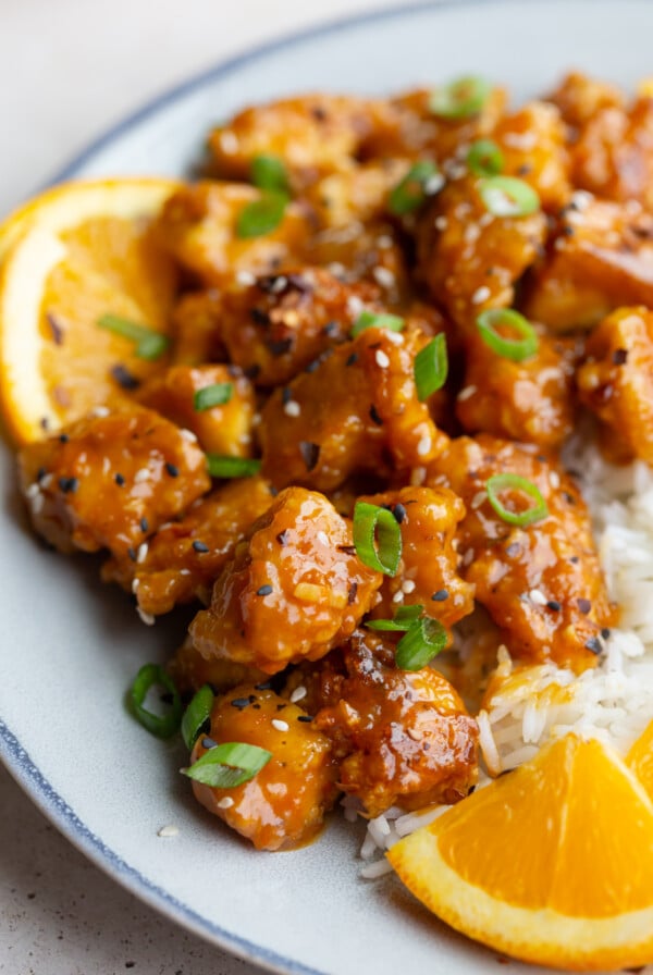 orange tofu on a plate with rice and orange slices