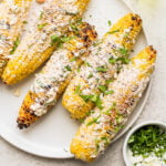 mexican street corn on the cobb with cheese and cilantro on top of it