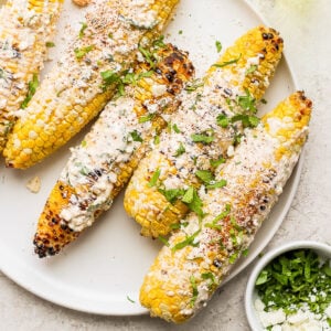 mexican street corn on the cobb with cheese and cilantro on top of it