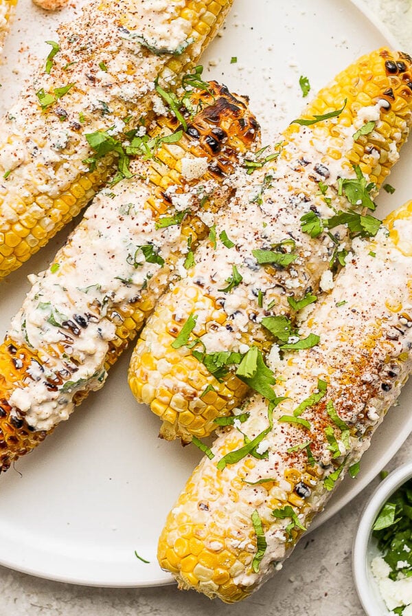 mexican street corn on the cobb with cheese and cilantro on top of it