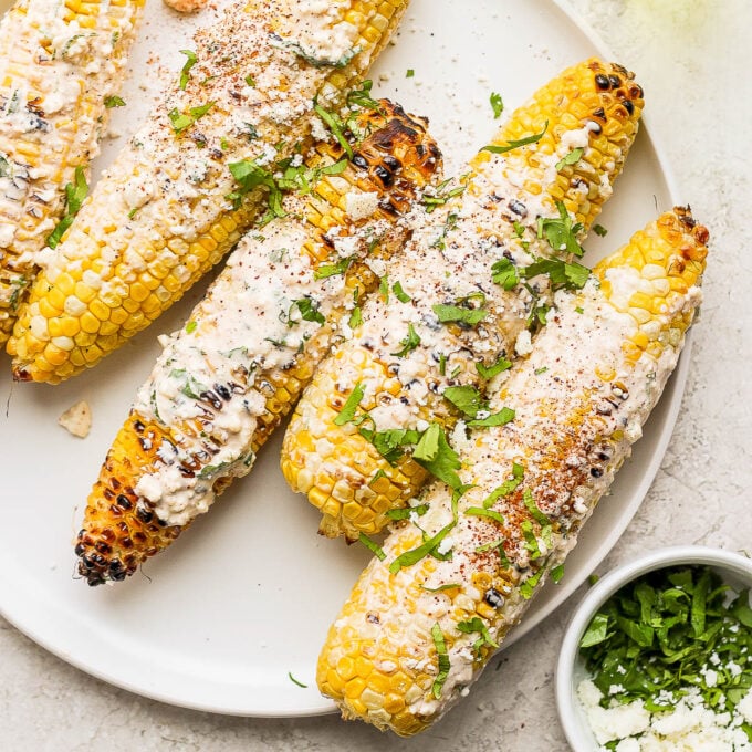 mexican street corn on the cobb with cheese and cilantro on top of it