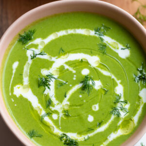 green goddess soup that's vibrant green in a pink bowl with a cream drizzle