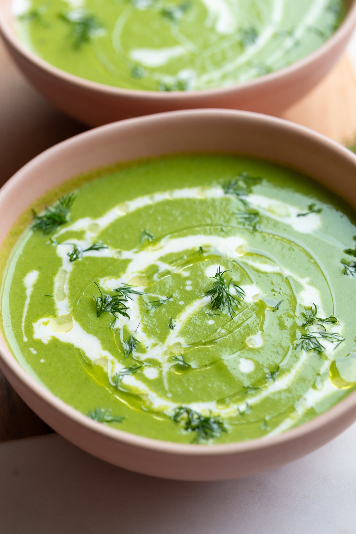 green goddess soup that's vibrant green in a pink bowl with a cream drizzle