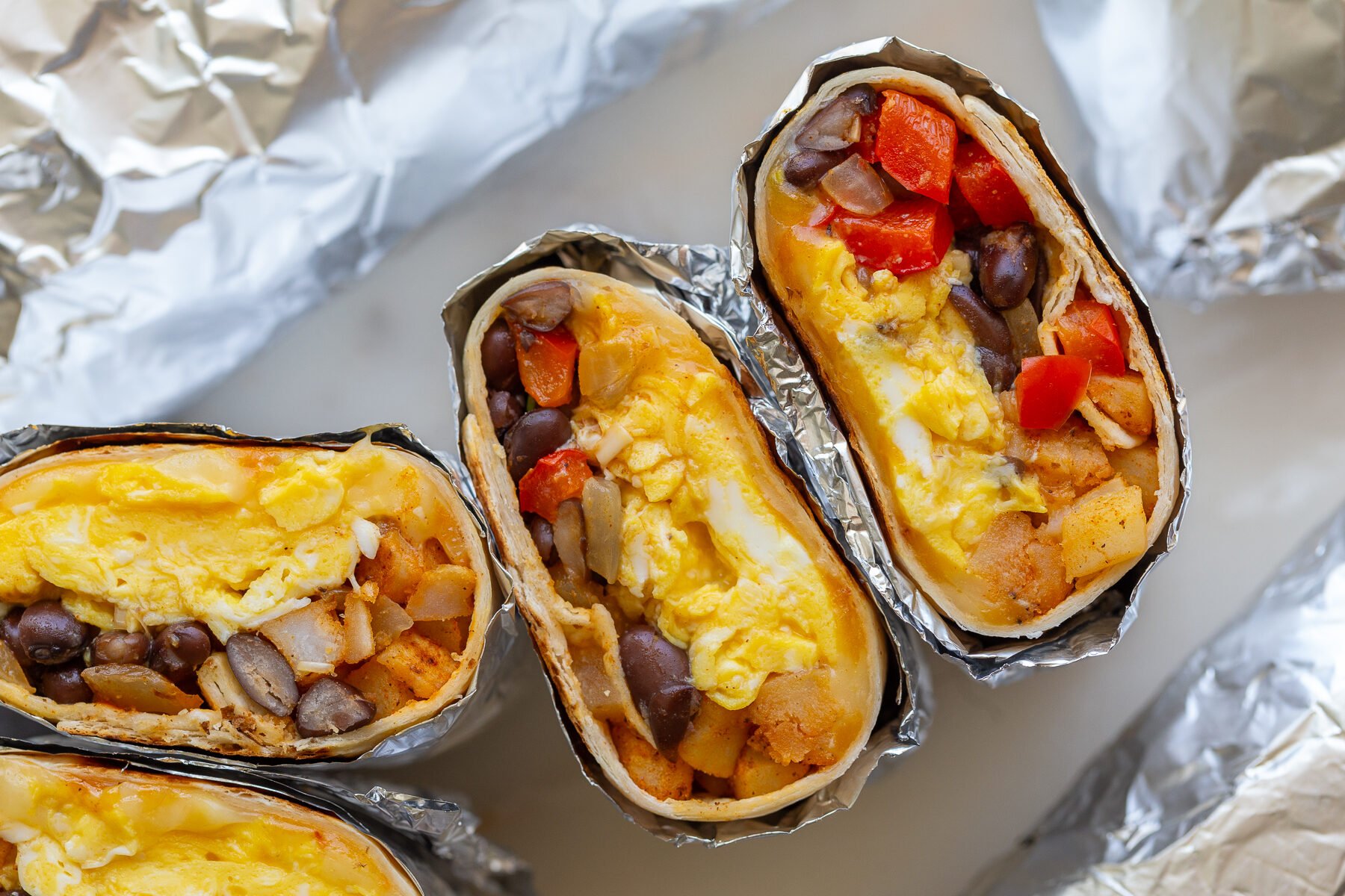 easy breakfast burrito recipe with 2 burritos cut open so you can seethe eggs, veggies and black beans inside
