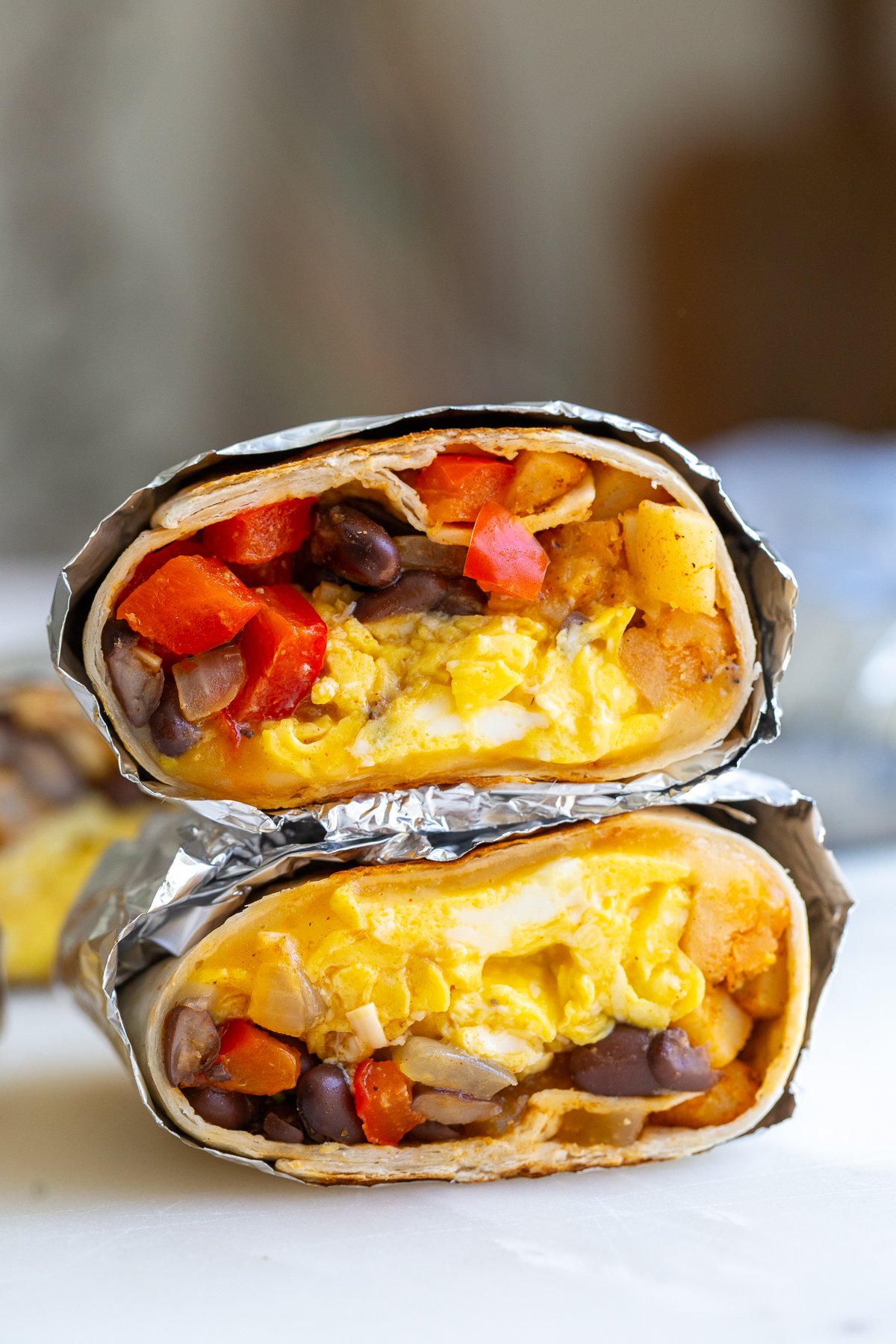 meatless breakfast burrito wrapped in foil and cut in half so you can see the inside with eggs, bell pepper, and black beans