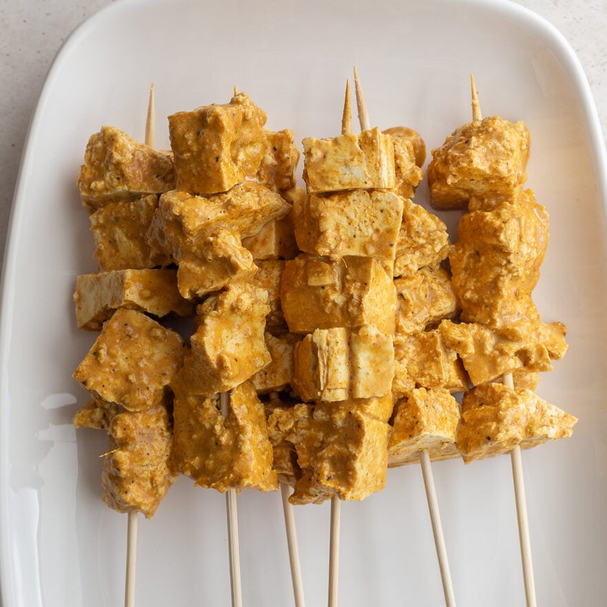 Marinated tofu on wooden skewers on a white serving platter.