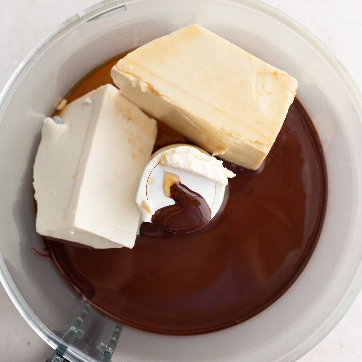 ingredients for tofu chocolate pudding in a food processor: silken tofu, maple syrup, melted chocolate