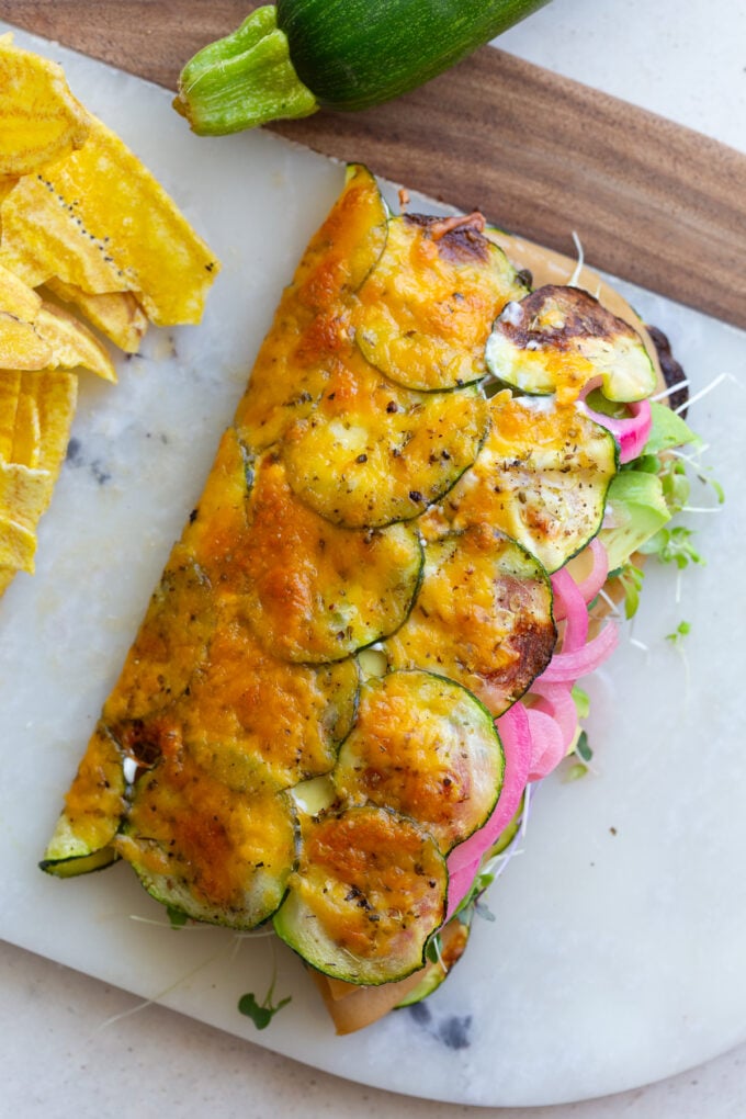 cheesy zucchini wrap stuffed with vegan meat, red onion, avocado and tomato. The wrap is on a plate with chips