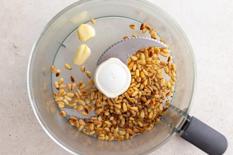 how to make pesto step 2: picture of a food processor with toasted pinenuts, lemon juice, and garlic cloves in it