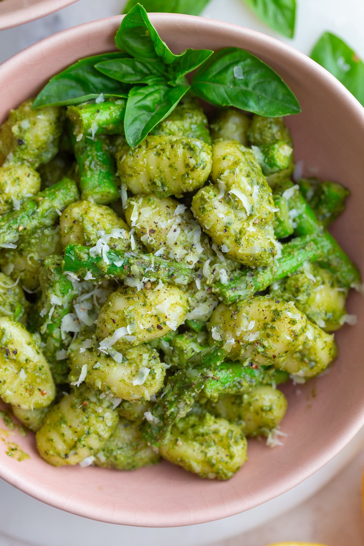 pesto gnocchi in a large bowl with fresh basil and lemon in the corners of the shot