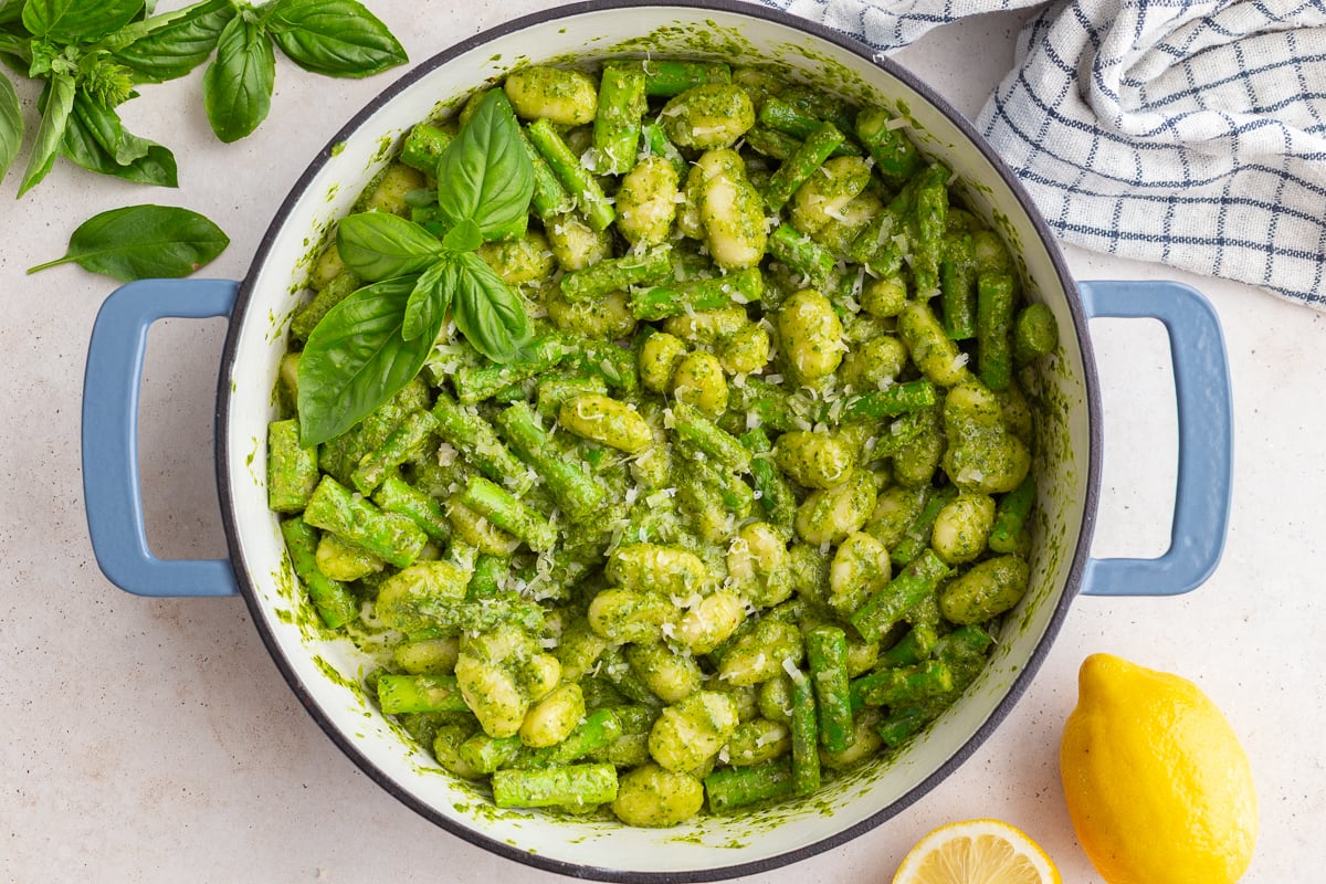 pesto gnocchi in a large skillet with fresh basil and lemon in the corners of the shot
