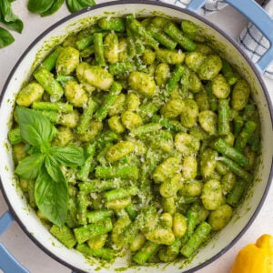 pesto gnocchi in a large skillet with fresh basil and lemon in the corners of the shot