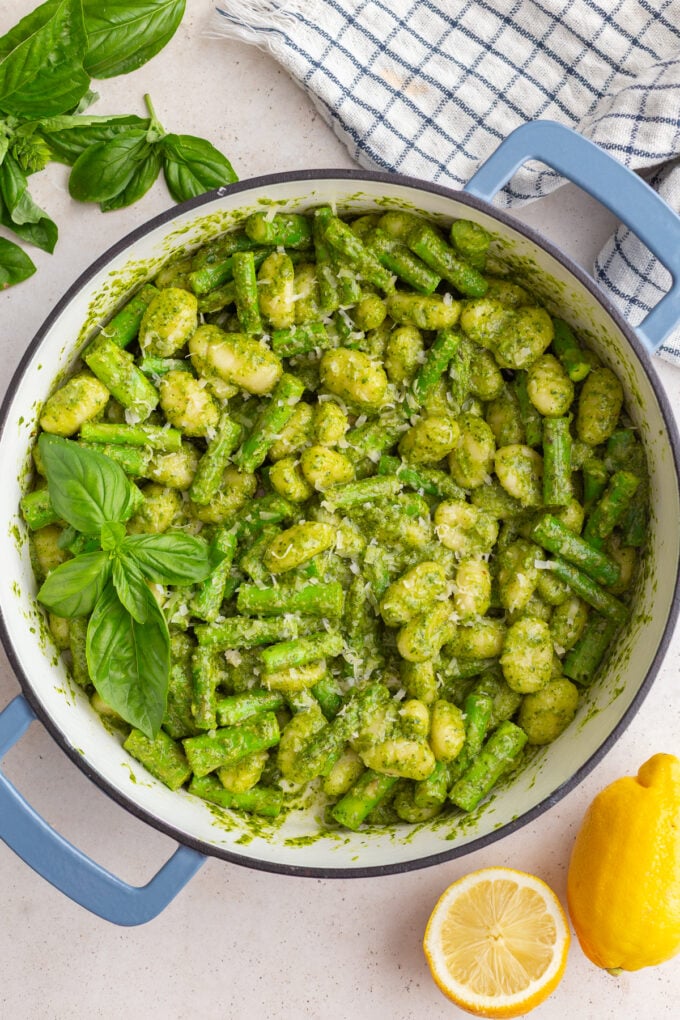 pesto gnocchi in a large skillet with fresh basil and lemon in the corners of the shot