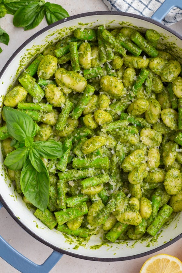 pesto gnocchi in a large skillet with fresh basil and lemon in the corners of the shot