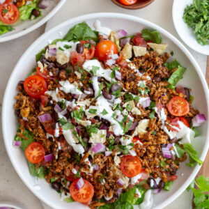 taco tofu rice bowls that is a large bowl of lettuce topped with rice, cherry tomatoes, crispy tofu taco meat, and drizzled with sour cream