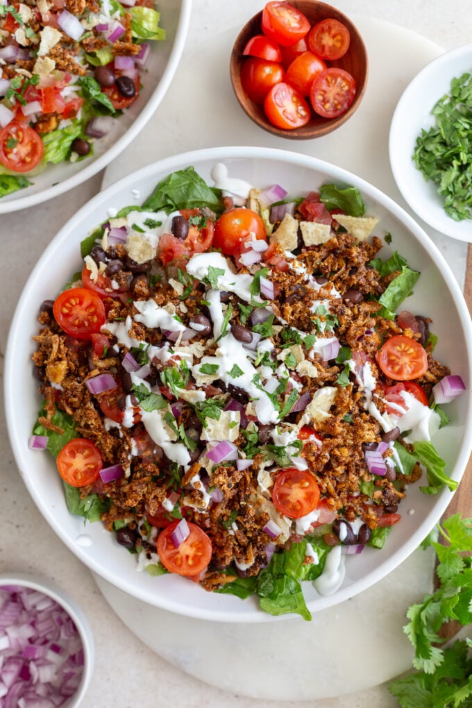 taco tofu rice bowls that is a large bowl of lettuce topped with rice, cherry tomatoes, crispy tofu taco meat, and drizzled with sour cream